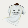 Real Madrid Home White Jersey 2526 Fans Version01 - KFCool – Football Jerseys & Soccer Kits Store White Real Madrid jersey featuring Emirates Fly Better sponsor and Adidas logo with yellow piping on a hanger (front view).
