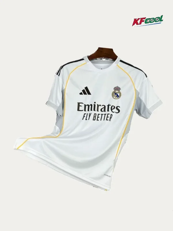 Real Madrid Home White Jersey 2526 Fans Version01 - KFCool – Football Jerseys & Soccer Kits Store White Real Madrid jersey featuring Emirates Fly Better sponsor and Adidas logo with yellow piping on a hanger (front view).