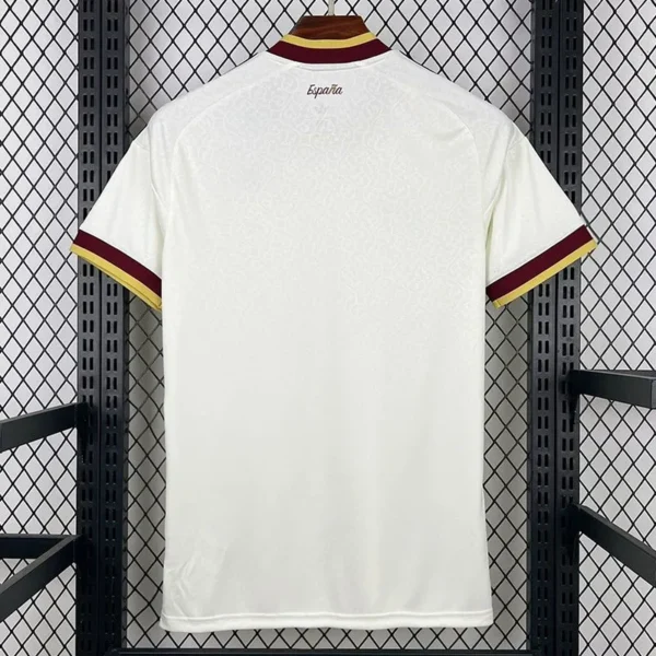 4f3bfd4cc995804f - KFCool – Football Jerseys & Soccer Kits Store Back view of a white soccer jersey hanging on a rack, with maroon and gold trim on cuffs and collar; small 'España' text near the neck.
