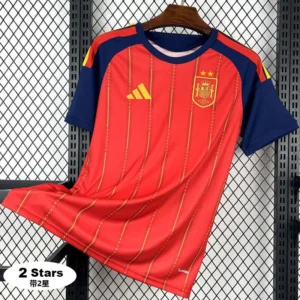 Red Spain national team jersey with yellow pinstripes and navy-blue sleeves, Adidas logo, crest with two stars, hanging on a wooden hanger against a metal grid background.