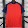 Red jersey with navy sleeves and yellow vertical stripes, back view, 'España' near the collar, hung on a wooden hanger.