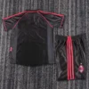 Black athletic jersey with red piping beside matching black shorts with red stripes and an AC Milan logo on the leg, laid flat on carpet.