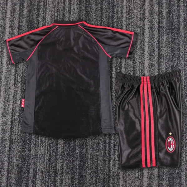 Black athletic jersey with red piping beside matching black shorts with red stripes and an AC Milan logo on the leg, laid flat on carpet.