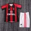 AC Milan soccer jersey with red and black vertical stripes and Opel sponsor, laid beside white shorts with red stripes on a gray carpet.