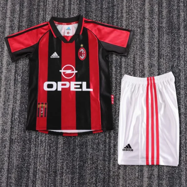 AC Milan soccer jersey with red and black vertical stripes and Opel sponsor, laid beside white shorts with red stripes on a gray carpet.