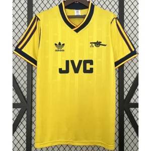 Arsenal 1986/88 Retro Away Jersey Fan Version - Front View Yellow Adidas soccer jersey with black stripes on sleeves, JVC sponsor, and cannon emblem on the chest, hanging on a hanger.