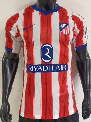Atlético Madrid soccer jersey on a mannequin with red and white vertical stripes, blue collar, crest, Nike logo, and Riyadh Air sponsor.