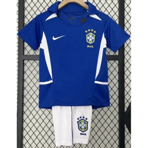 Blue Brazil national team jersey with white accents and crest, paired with white shorts featuring the Brazilian badge, hanging on a hanger in front of a fence.