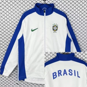 Brazil 1998/99 Retro White Windbreaker - Front View White Brazil track jacket with blue sleeves and zipper; green Nike swoosh on left chest and Brazil crest on right chest, standing against a chain-link background.