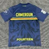 Blue Cameroon football jersey viewed from the back with yellow CAMEROUN lettering, a red-yellow-green stripe, and a dark abstract pattern; 'FOURTEEN' at the bottom.