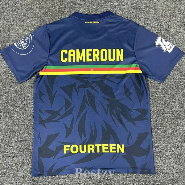 Blue Cameroon football jersey viewed from the back with yellow CAMEROUN lettering, a red-yellow-green stripe, and a dark abstract pattern; 'FOURTEEN' at the bottom.