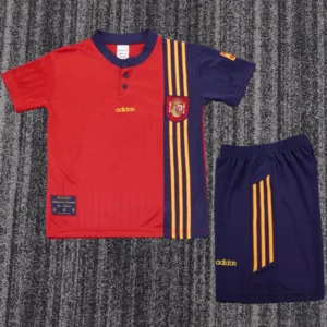 Red and navy Spain national team football jersey with yellow stripes and crest, paired with navy shorts.