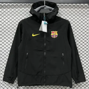 Black zip-up jacket with FC Barcelona crest and yellow Nike swoosh on chest, hanging on a display hanger with tags attached.
