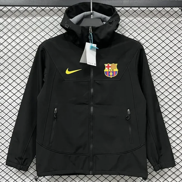 Black zip-up jacket with FC Barcelona crest and yellow Nike swoosh on chest, hanging on a display hanger with tags attached.
