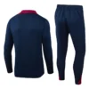 Back view of a navy blue tracksuit jacket with a red collar paired with matching navy pants that have red accents at the cuffs/ankles.