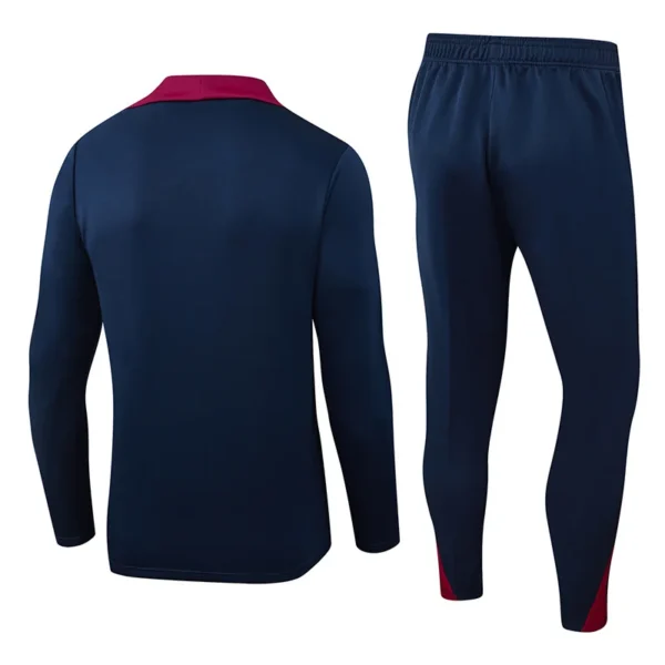 Back view of a navy blue tracksuit jacket with a red collar paired with matching navy pants that have red accents at the cuffs/ankles.