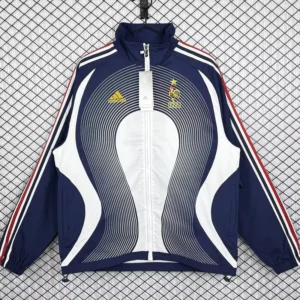 Navy blue Adidas France national team training jacket with white center panels, red stripes on sleeves, hanging on a grid-pattern backdrop.
