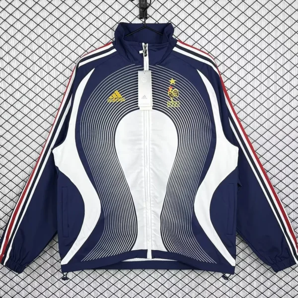Navy blue Adidas France national team training jacket with white center panels, red stripes on sleeves, hanging on a grid-pattern backdrop.