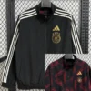 Black Adidas track jacket with white three-stripe sleeves and gold German national team crest on the left chest; zip front, elastic hem.