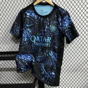 Inter Milan football jersey in black with blue abstract pattern, Qatar Airways sponsor, hanging on a hanger against a chain-link fence.