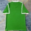 Green short-sleeve sports jersey with white trim on sleeves, laid flat on a rug surface.