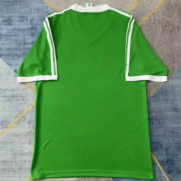 Green short-sleeve sports jersey with white trim on sleeves, laid flat on a rug surface.