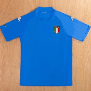 Blue Italy national football team jersey laid flat, with Italia crest on the chest, Kappa logos on the sleeves, and two yellow stars on the left sleeve.