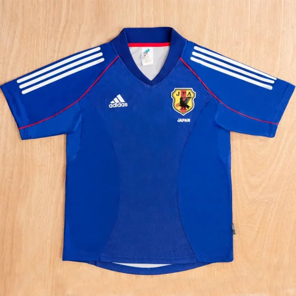 Blue Japan national football jersey laid flat, featuring Adidas logo and JFA crest with three white stripes on the sleeves.