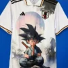 White Japan soccer jersey with Adidas stripes and crest, featuring a large Dragon Ball Z character (Goku) meditating with a pastel sun background.