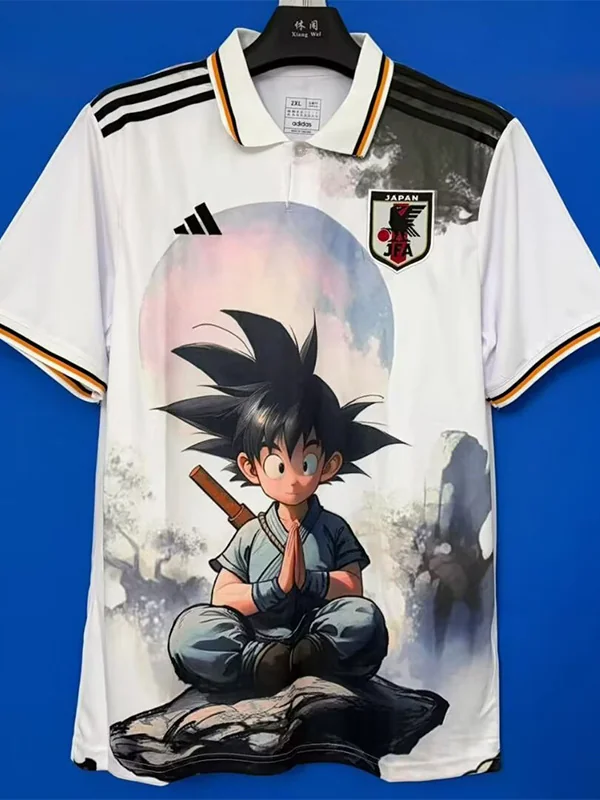 White Japan soccer jersey with Adidas stripes and crest, featuring a large Dragon Ball Z character (Goku) meditating with a pastel sun background.
