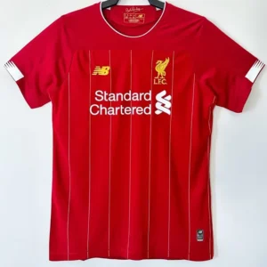 Liverpool 2019/20 Home Jersey Fan Version - Front View Red Liverpool FC home jersey with white pinstripes, club crest, and Standard Chartered sponsor logo on the chest, hanging on a hanger.
