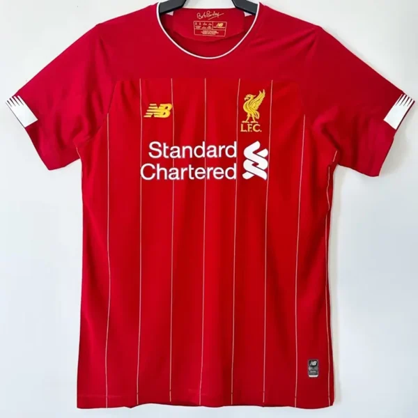 Liverpool 2019/20 Home Jersey Fan Version - Front View Red Liverpool FC home jersey with white pinstripes, club crest, and Standard Chartered sponsor logo on the chest, hanging on a hanger.
