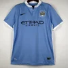 Light blue Manchester City home jersey on a hanger, featuring Nike swoosh and club crest with Etihad Airways sponsor.