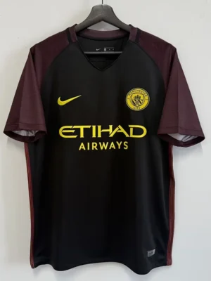 Black Manchester City jersey with maroon sleeves on a hanger; yellow Nike swoosh, club crest, and Etihad Airways sponsor.