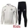 Manchester City 2026/27 Kids Jacket Tracksuit - Front View - KFCool – Football Jerseys & Soccer Kits Store Kids' white and black tracksuit set with Manchester City logos, featuring a white zip jacket and black pants with decorative side stripes.