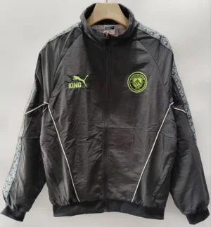 Black Manchester City track jacket on a hanger, with neon crest on the left chest, neon Puma King logo on the right, white piping, and a patterned sleeve design.