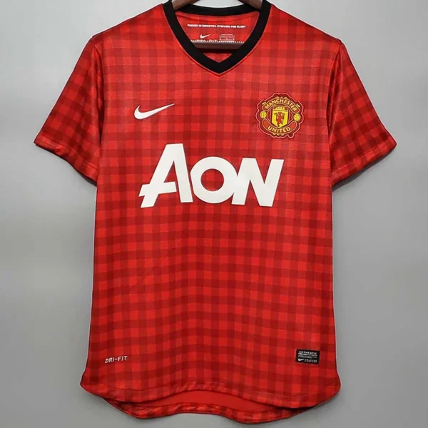 Manchester United 2012/13 Retro Home Jersey Fan Version - Front View Manchester United red home jersey on a hanger with checkered pattern, crest, Nike swoosh, and AON sponsor logo.
