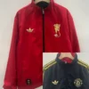 Manchester United 2025/26 Double Sided Windbreaker - Front View - KFCool – Football Jerseys & Soccer Kits Store Red zip-up jacket with gold crest on left chest and Adidas trefoil on the right, hanging on a wooden hanger.