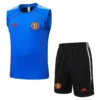 Manchester United blue training jersey with crest and red Adidas logo, shown with black shorts featuring the club crest and white stripes.