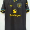 Manchester United black away jersey with yellow trim and Snapdragon sponsor on chest, hanging on a hanger
