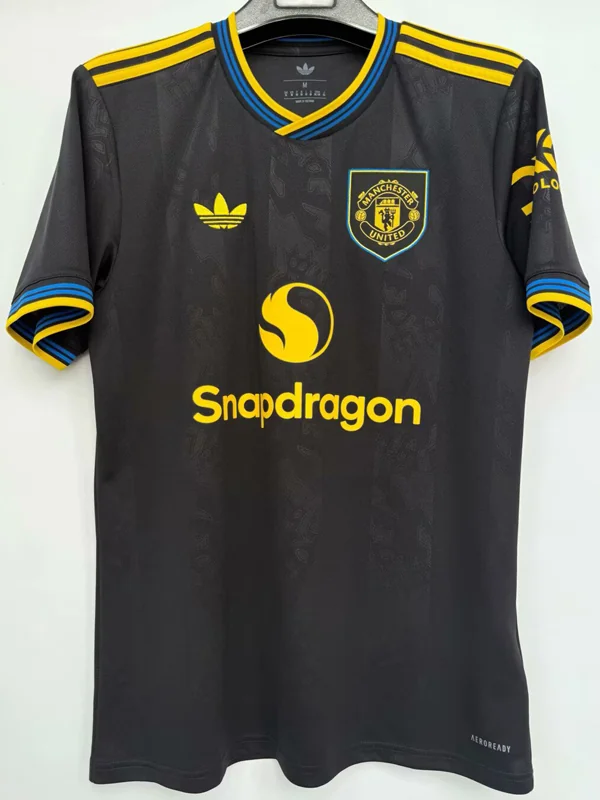 Manchester United black away jersey with yellow trim and Snapdragon sponsor on chest, hanging on a hanger