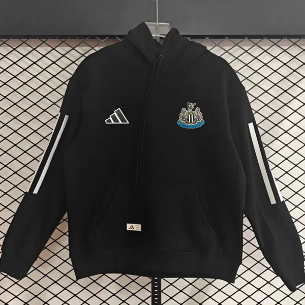 Black Adidas hoodie featuring a Newcastle United crest on the chest, white sleeve stripes, front pocket, hanging on a display against a grid backdrop.