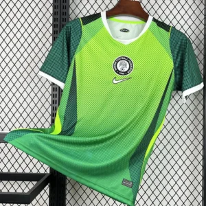 Nigeria 2026/27 Home Jersey Fan Version - Front View Bright green football jersey with white trim and Nike swoosh, hanging on a wooden hanger in front of a metal grid background.