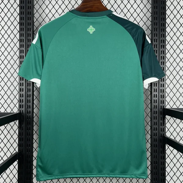 Northern Ireland 2026/27 Home Jersey Fan Version - Back View Back view of a green athletic jersey with dark green sleeves and white cuffs, hanging on a wooden hanger in a metal rack; small emblem on the upper back.