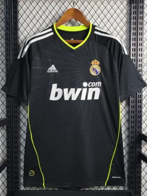 Real Madrid football jersey in black with neon lime piping on a hanger, featuring sponsor bwin and club crest.