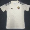 White AS Roma football jersey with dark side panels, three black stripes on shoulders, and club crest on the chest laid flat.