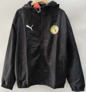 Senegal 2026/27 Windbreaker - Front View Black zip-up windbreaker with a hood, featuring a white Puma logo on the left chest and a circular colorful crest on the right chest with two stars above it.